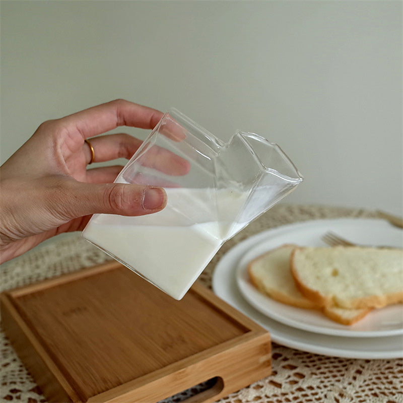 Holding a unique glass carton of milk, perfect for adding a creative touch to your table. Nest Haven Shop, GLASS, KITCHEN