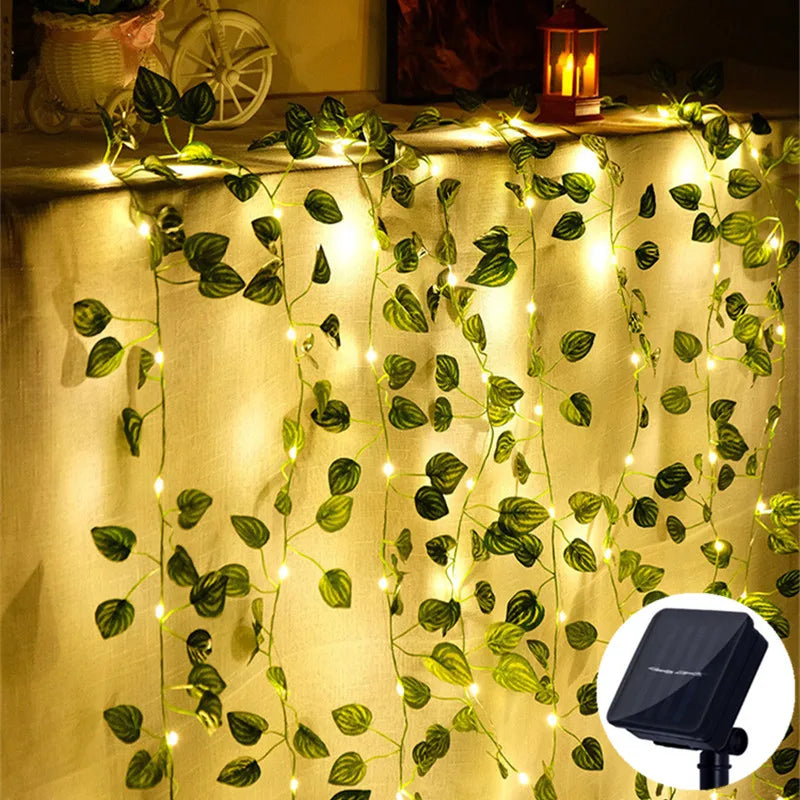 Leaf garland with fairy lights adding a magical glow to any setting, perfect for evening gatherings indoors or out. Lush greenery and twinkling lights for an elegant, charming decor. Solar-powered. Nest Haven Shop, GARDEN