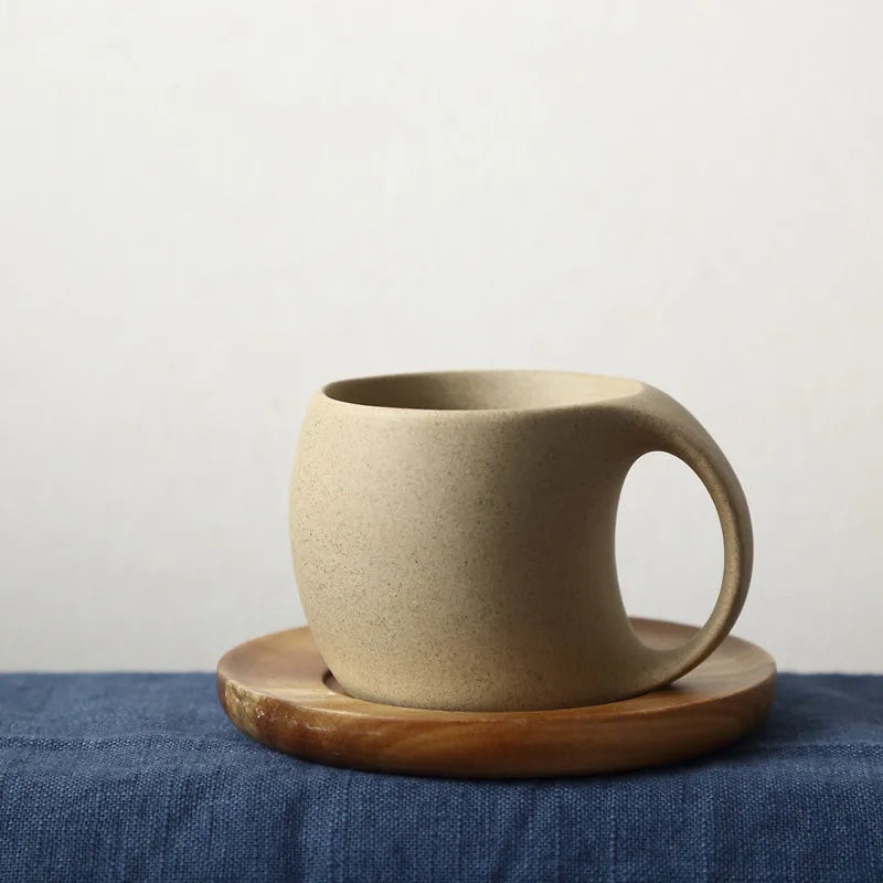 Rustic ceramic coffee cup with unique handle on wooden saucer, perfect for cozy drinks or decor from Nest Haven Shop, KITCHEN.