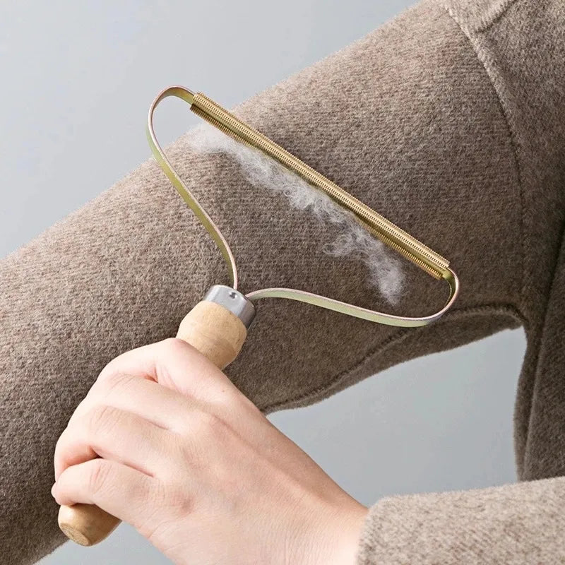 Elegant lint remover with a metal handle and wooden grip, being used on a brown sweater to remove fuzz and pilling. Nest Haven Shop.