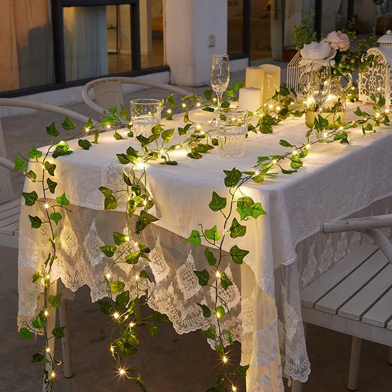 Leaf garland with fairy lights adding a magical touch to an evening table setup, draped over a lace tablecloth for elegant decor - Nest Haven Shop, GARDEN